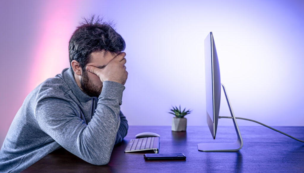 tired-man-sits-front-computer-covering-his-face-with-his-hands-1024x585 Burnout e Cultura da Produtividade: Como o Excesso de Trabalho Afeta a Saúde Mental
